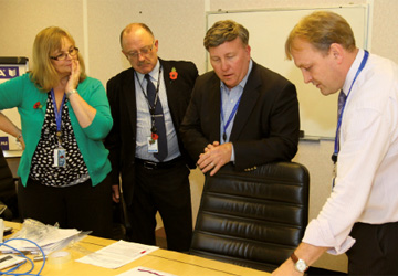 four business people standing around a desk discussing what is on it 