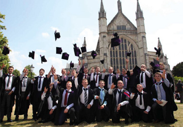 students at a graduation wearing robes and throwing mortar boards in front of a cathedral  