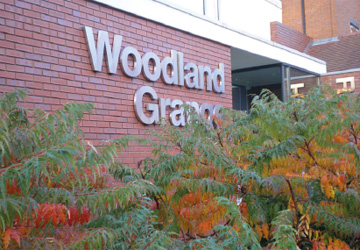 A sign saying Woodland Grange mounted on a brick wall with ferns in the foreground