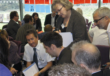 a room full of people, some sitting, some standing leaning towards the centre having a discussion