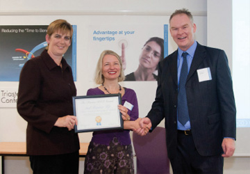 two women and a men in business dress shaking hands - the woman in the middle is holding a certificate