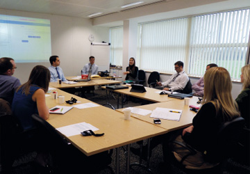 people in business dress sitting around a large desk 