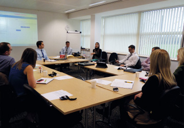 people in business dress sitting around a O shaped desk