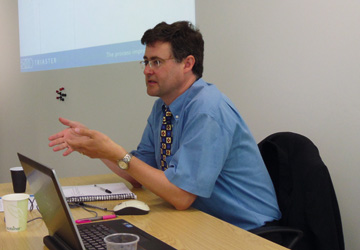 a man in a blue shirt sitting at a desk in front of a projection