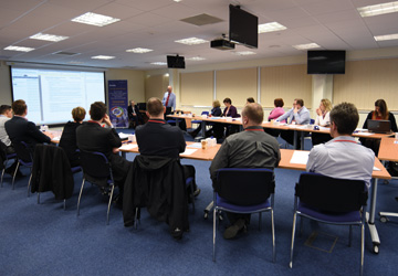 people in a business dress seated around a desk looking at a projector screen