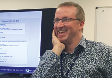 a close up of a man in a blue shirt with glasses laughing 