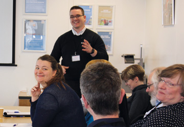 a man in a blue jumper behind a group of people sat down