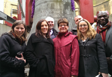 a group of people in coats standing in front of a big metal bell 