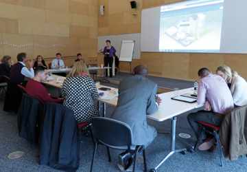 people sitting around a U shaped desk looking at a projected image 