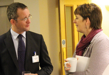 a man in a suit talking to a woman with short hair and a purple scarf