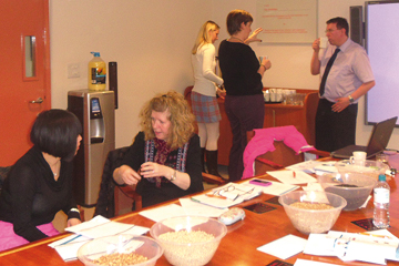 a room full of people in business dress some stood up some sat down around a desk with food on it, chatting to each other