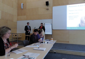 people sitting at a desk watching a woman and a man presenting