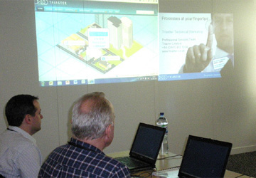 2 men at a desk with laptops open looking at a projection on screen