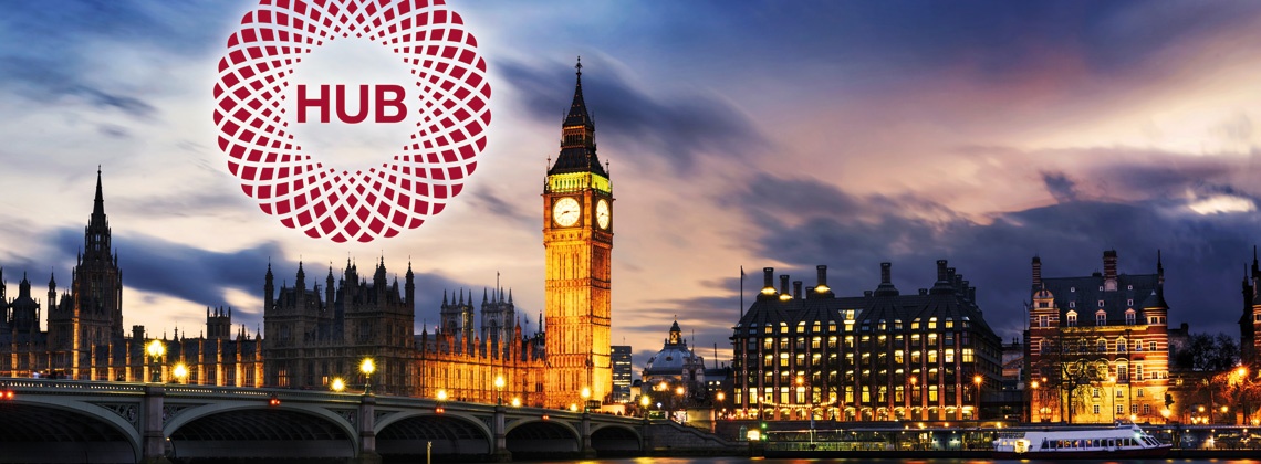 The houses of parliament at night with the lights on and a circle with HUB written in red in the sky