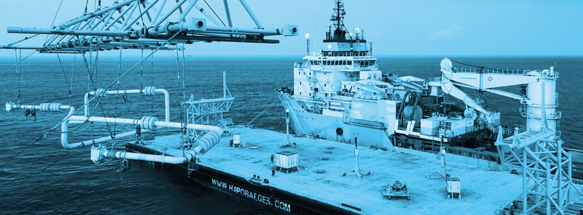 A ship at sea docking next to a platform with cranes attached with a blue filter
