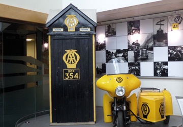 a black door with the AA written on it in yellow writing, next to a yellow motorbike and sidecar